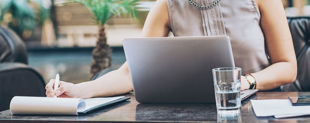 woman sitting at a laptop while writing on a legal notepad