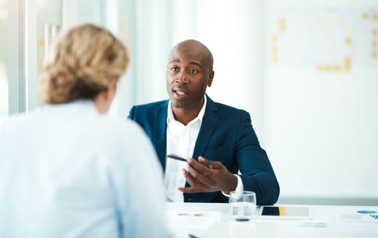 header image of lawyer behind table holding pin talking to client facing away from camera