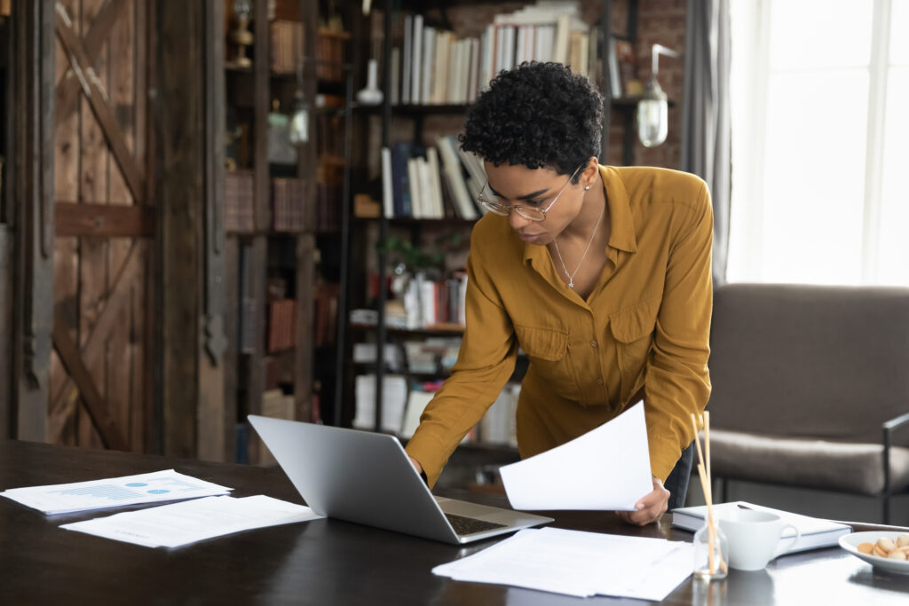 header image of women standing over desk with piles of paper around a laptop