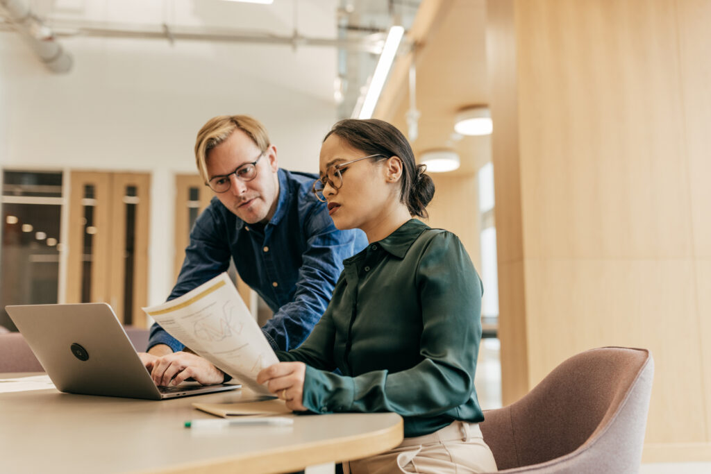 header image of man standing behind and talking to women holding paper at desk