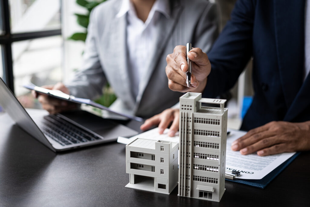 header image of two people behind desk pointing to a model of an apartment building on the desk